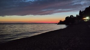 A beach at dusk with a calm sea and a sunset sky. - Cliff House with beautiful sea view. Panoramic views just infront of our terrace (Krstac)