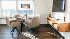Et moderne spiseområde med et rundt bord, fire stole, en pendel og et fjernsyn monteret på væggen.
