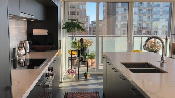 A modern kitchen with a central island, built-in appliances, and a view of the city through large windows. - Beautiful Light-filled Apartment with Spectacular Views of Toronto (Toronto)