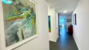 A hallway with a large abstract painting on the left, a door leading to a room with a piano, and a view of a cityscape through a window. - Beautiful Light-filled Apartment with Spectacular Views of Toronto (Toronto)