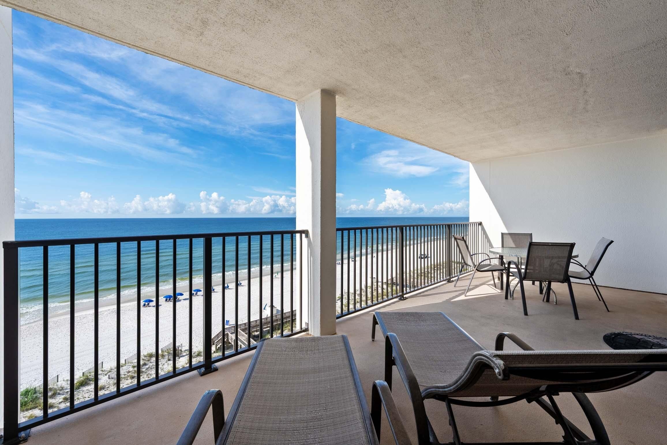 A balcony with a view of a beach and ocean, featuring a table and chairs.
