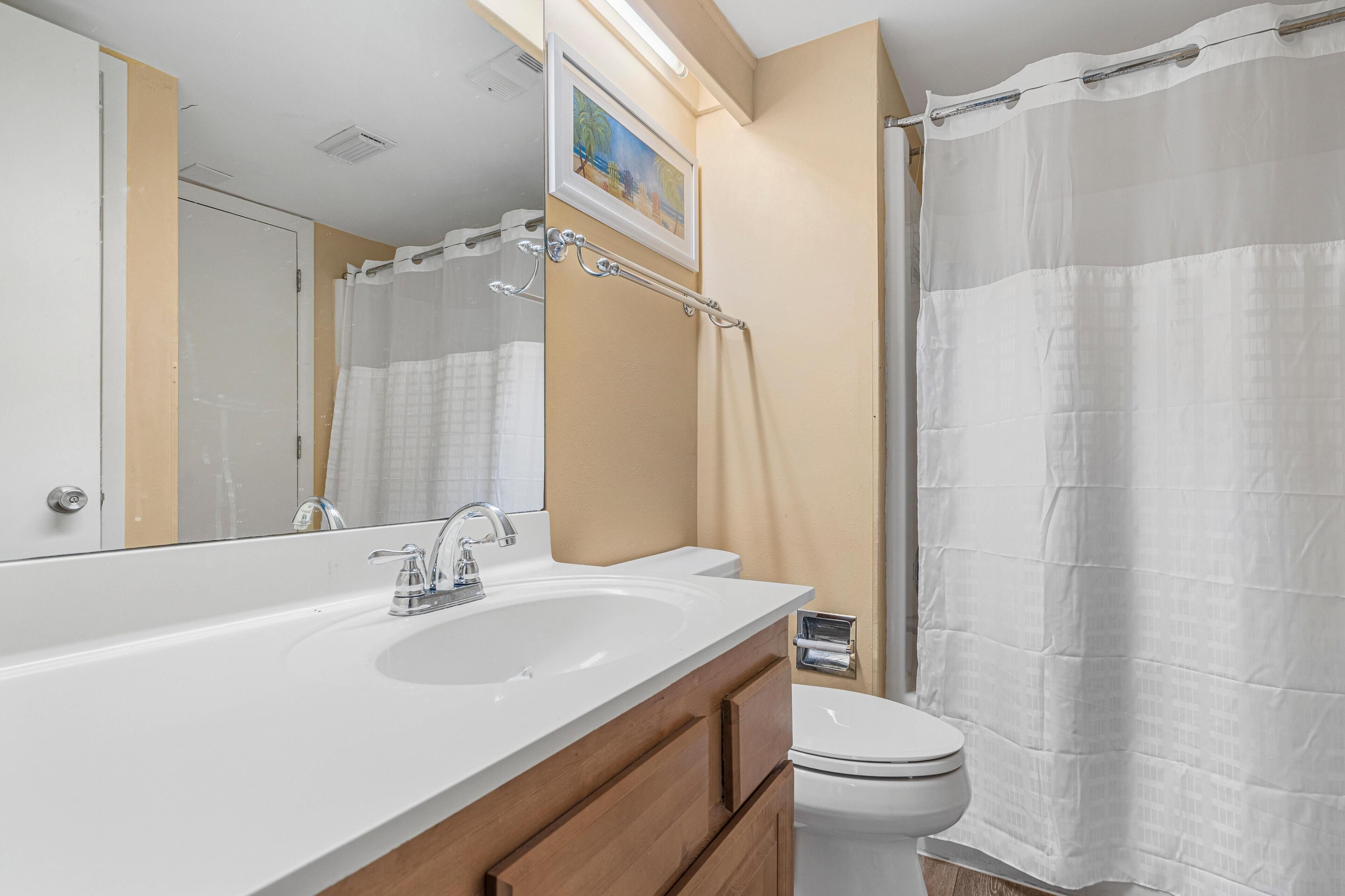 Un baño con lavamanos blanco, espejo y retrete, paredes color beige y cortina de ducha.