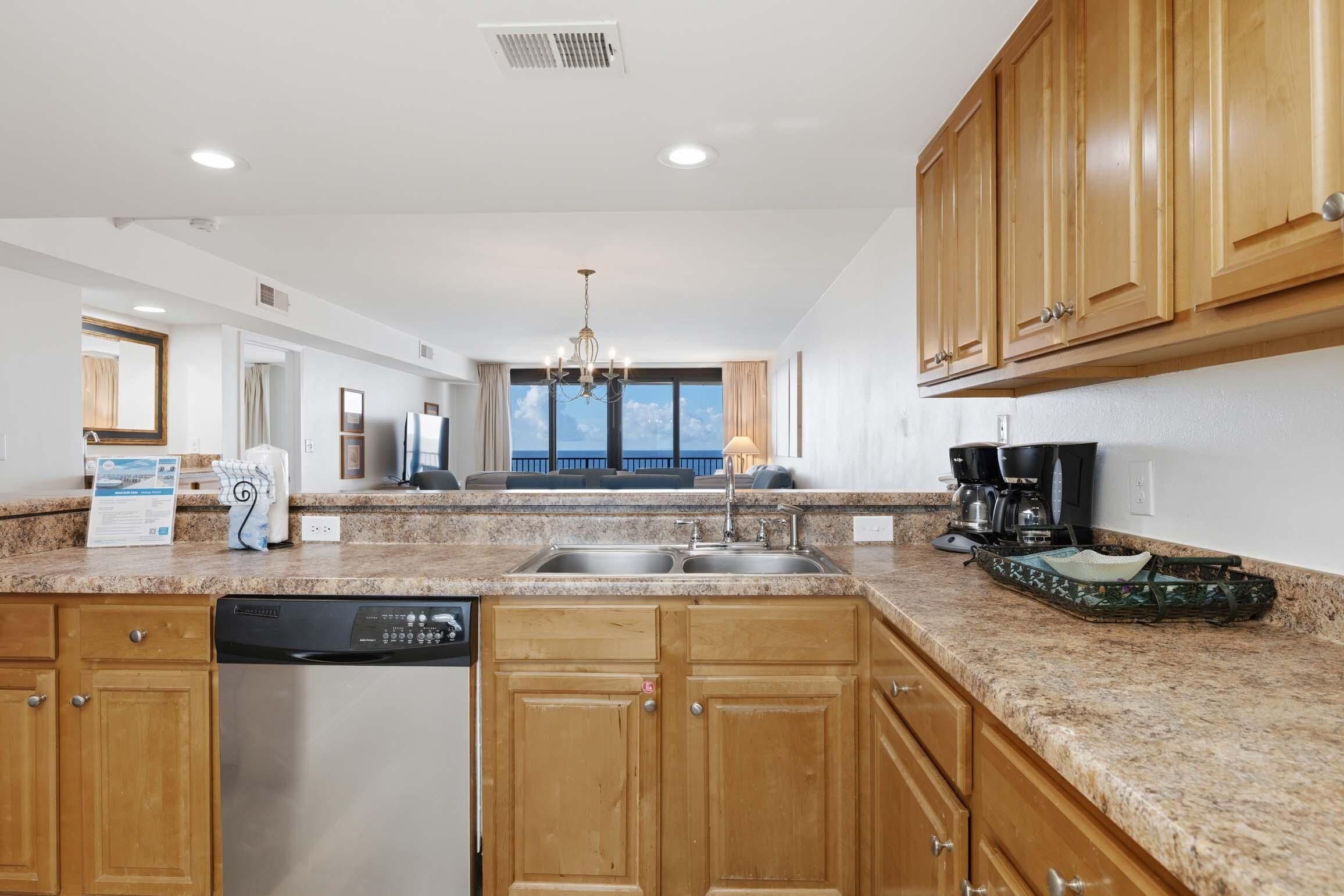 A modern kitchen with granite countertops, wooden cabinets, a dishwasher, and a coffee maker.