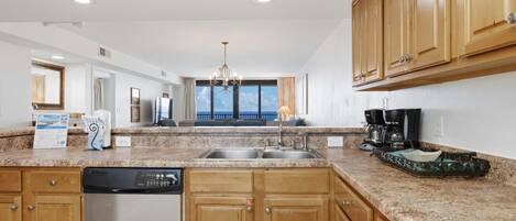 A modern kitchen with granite countertops, wooden cabinets, a dishwasher, and a coffee maker.