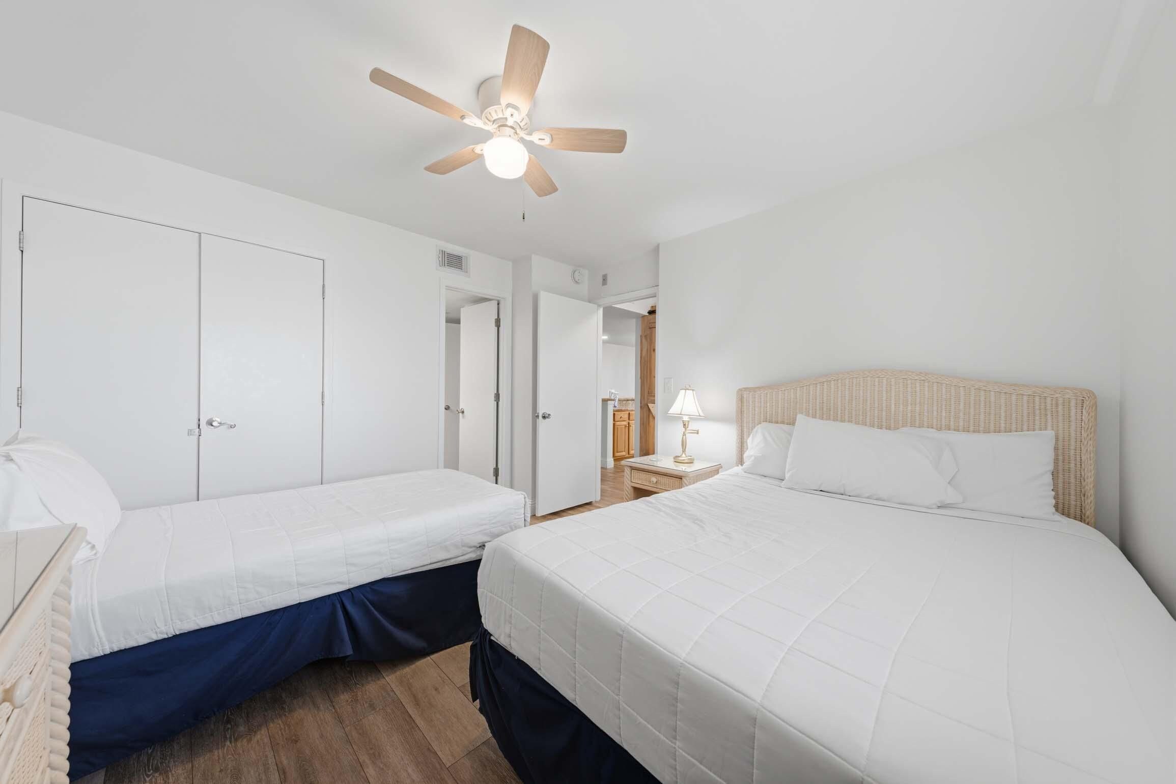 Quarto de hotel com duas camas de solteiro, um ventilador de teto e uma pequena mesa com abajur.