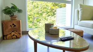 Ein modernes Wohnzimmer mit einem Glastisch, einem weißen Sofa und Blick auf Grün.