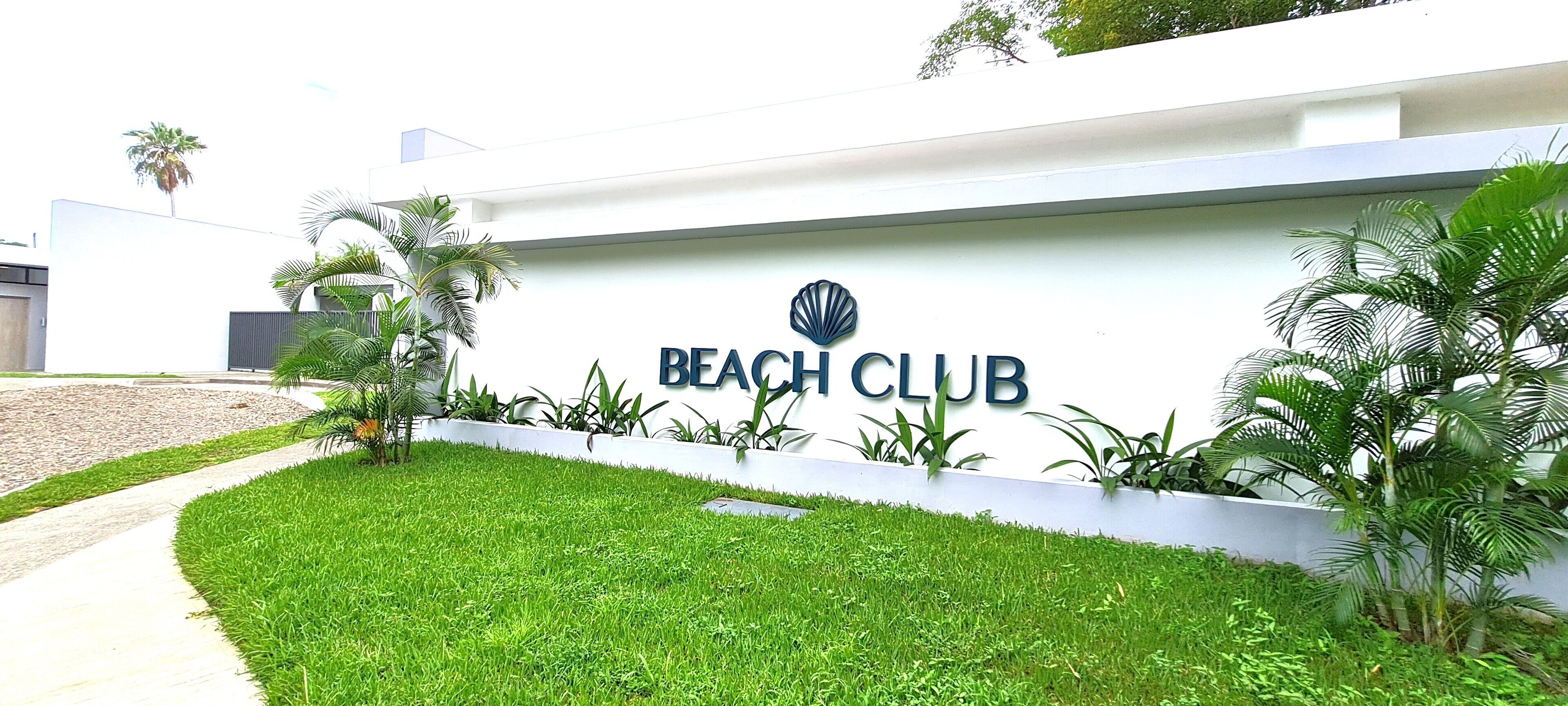 A sign for the Beach Club with a modern design, surrounded by well-maintained grass and palm trees.