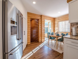 A modern kitchen with a stainless steel refrigerator, wooden walls, a dining area with a table and chairs, and a view through the window. - The Cabin: Private Pool, Luxury Log Home (Grand Junction)