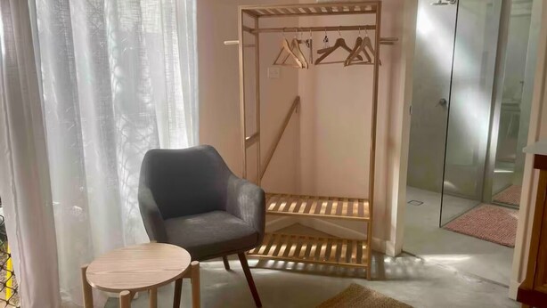A room with a grey armchair, a small round table, a wooden hanging rack, and a glass shower enclosure. - Adorable 1br apt walking distance to Mullumbimby (Mullumbimby)