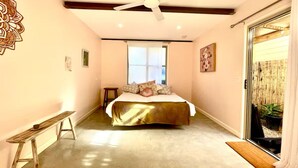 A bedroom with a bed, a ceiling fan, a bench, and a sliding glass door leading to a balcony with a bamboo fence. - Adorable 1br apt walking distance to Mullumbimby (Mullumbimby)