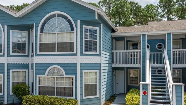 A two-story building with a blue exterior and white trim. It features a balcony on the second floor and a staircase leading to the entrance. - Villas at Island Club Community, pools, jacuzzi and more! (Kissimmee)
