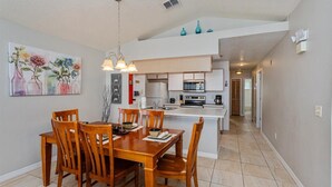 A modern kitchen with white cabinets, a central island, and a dining area with wooden chairs and a table. - Villas at Island Club Community, pools, jacuzzi and more! (Kissimmee)