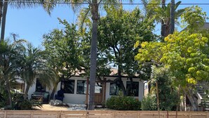 A residential property with a wooden fence, palm trees, and a house with large windows. - Cottage by the Harbor (Dana Point)
