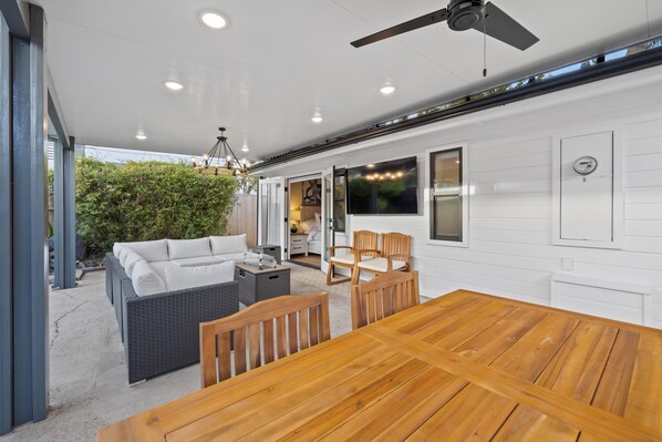 An outdoor dining area with a wooden table and chairs, a wicker sofa, and a ceiling fan. - Cottage by the Harbor (Dana Point)