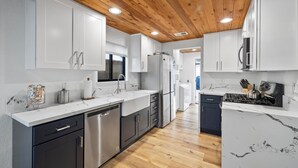 A modern kitchen with white cabinets, a wooden ceiling, and a marble countertop. - Cottage by the Harbor (Dana Point)