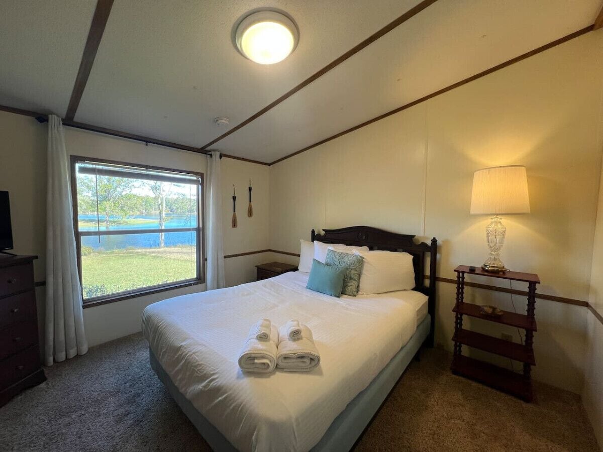 A neatly made bed with pillows and towels, a bedside lamp, and a window with curtains.