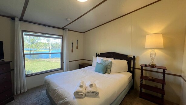 A neatly made bed with pillows and towels, a bedside lamp, and a window with curtains.