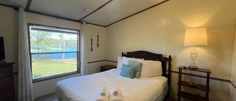 A neatly made bed with pillows and towels, a bedside lamp, and a window with curtains.