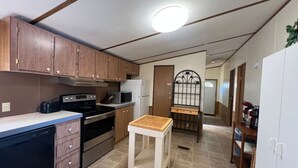 A compact kitchen with wooden cabinets, a dishwasher, a stove, and a small wooden table.