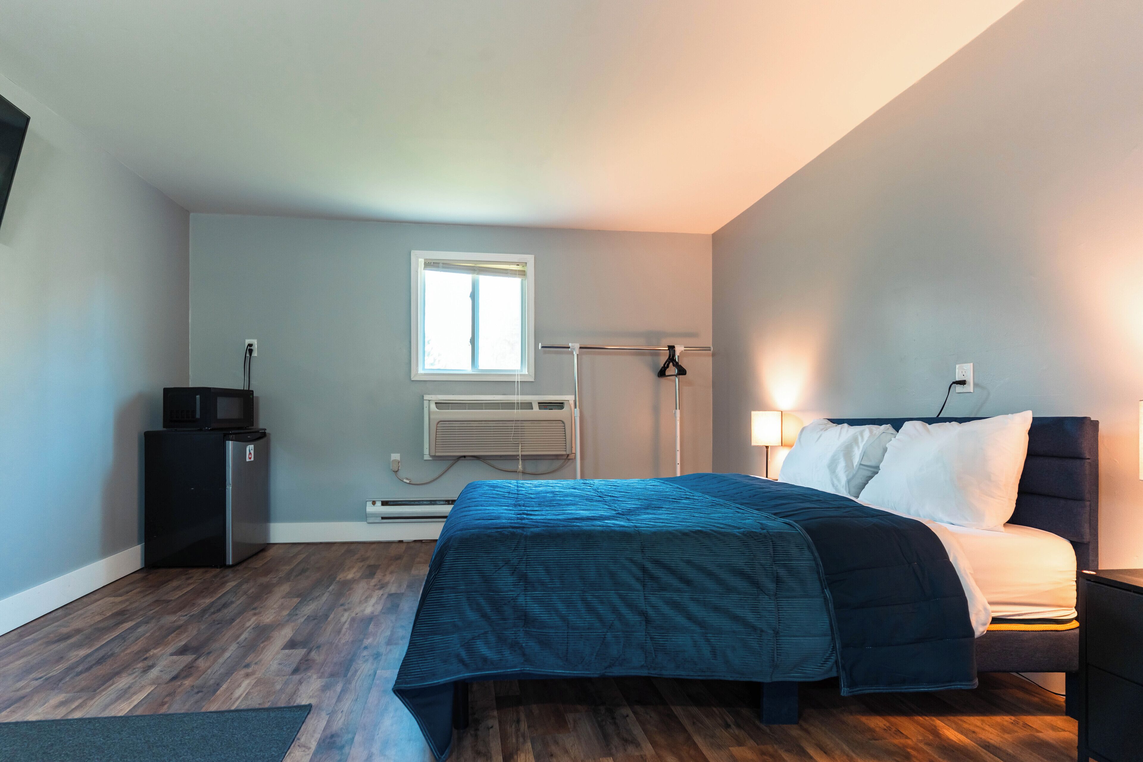 Une chambre à coucher comprenant un lit, un bureau, une chaise, une fenêtre et un appareil de climatisation.