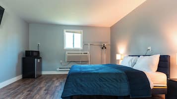 Une chambre à coucher comprenant un lit, un bureau, une chaise, une fenêtre et un appareil de climatisation.