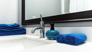 Un bagno con un lavandino bianco, un rubinetto moderno e un dispenser di sapone blu.