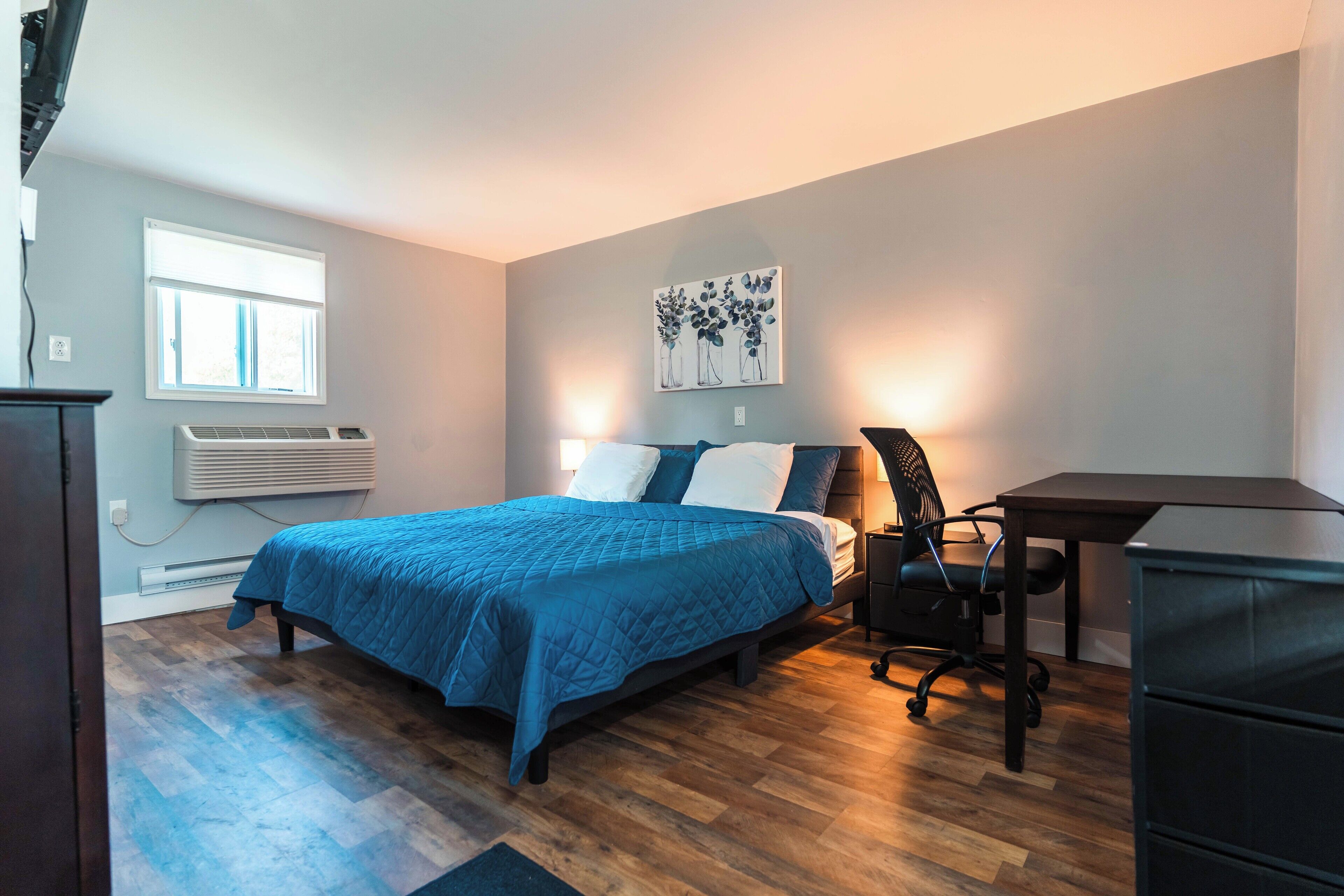 Un dormitorio con cama, escritorio, silla, calentador y ventana.