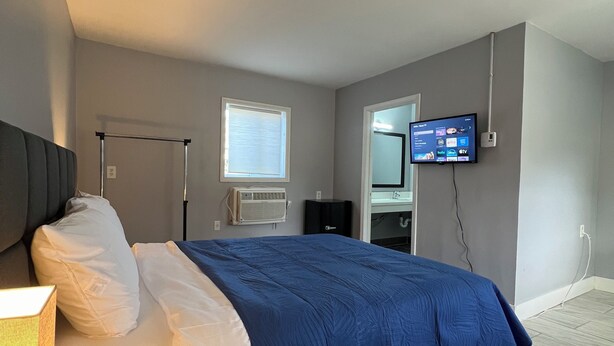 Camera da letto moderna con letto, lampada da comodino, condizionatore d'aria e televisore a parete che mostra l'interfaccia di un servizio di streaming.