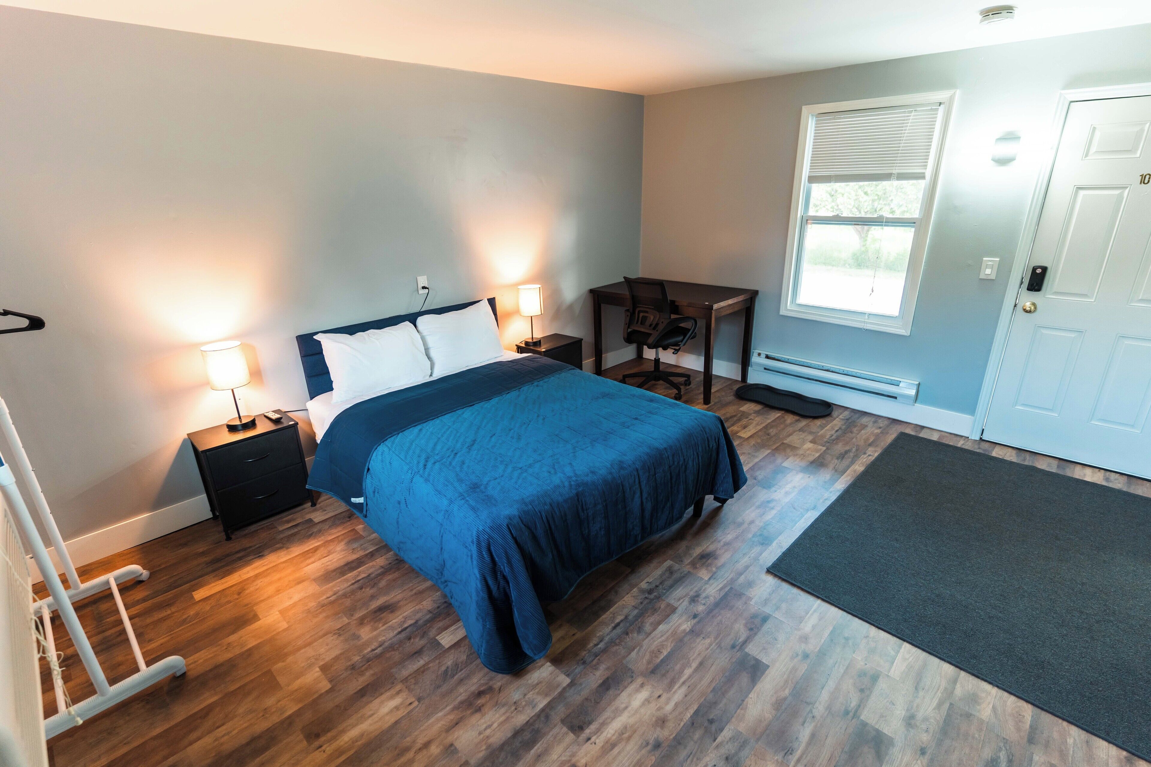 A bedroom with a bed, bedside tables, a desk, and a window.
