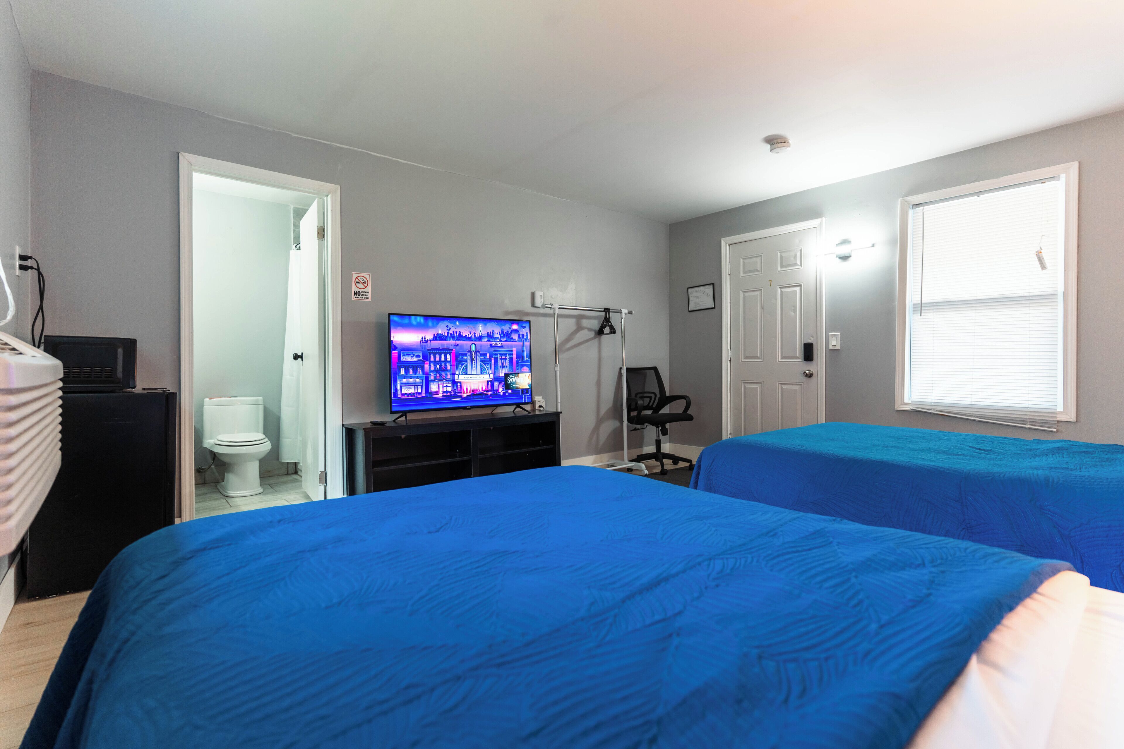 A bedroom with two beds, a TV, a desk, and a door leading to a bathroom.