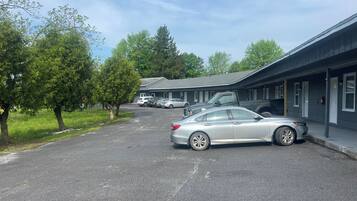 A motel with a parking lot, several cars parked, and trees lining the street.