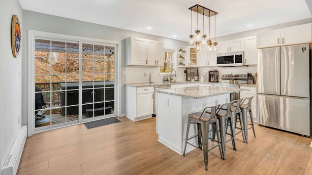 A modern kitchen with white cabinets, stainless steel appliances, and a large island with bar stools. - BlueStone Retreat w/ HotTub & Game Room in Poconos (Coolbaugh Township)
