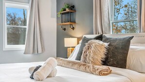 A neatly made bed with a fluffy pillow and rolled towels, a bedside lamp, and a wall-mounted shelf with a plant. - BlueStone Retreat w/ HotTub & Game Room in Poconos (Coolbaugh Township)