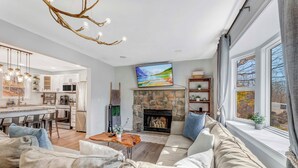 A modern living room with a stone fireplace, a large TV mounted above it, and a cozy seating area. - BlueStone Retreat w/ HotTub & Game Room in Poconos (Coolbaugh Township)