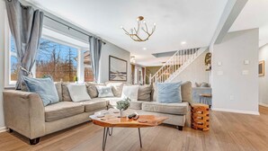 A modern living room with a sectional sofa, a wooden coffee table, and a staircase leading to an upper level. - BlueStone Retreat w/ HotTub & Game Room in Poconos (Coolbaugh Township)