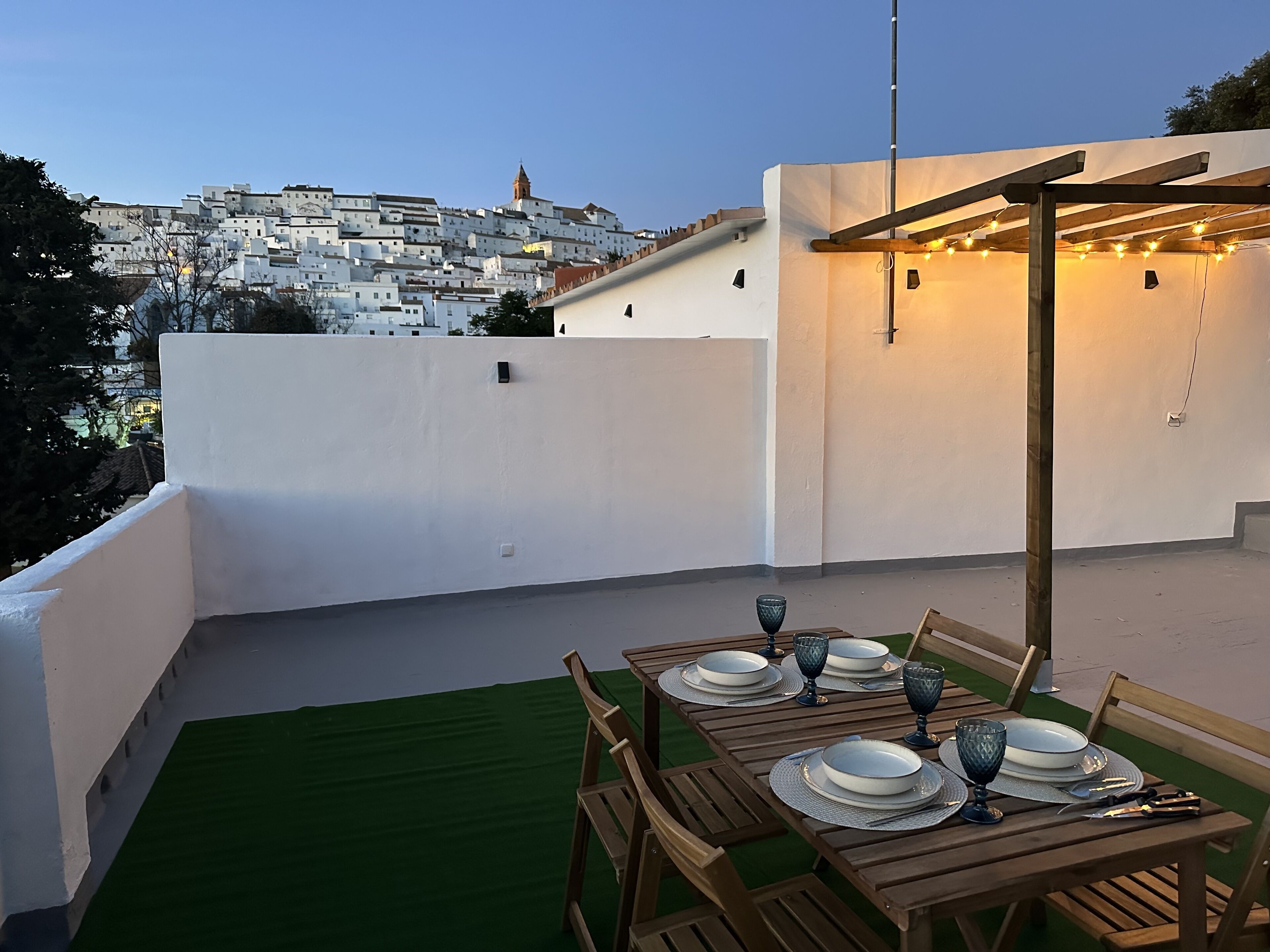 Terraza en la azotea con una mesa lista para cenar, con vistas a un paisaje urbano.