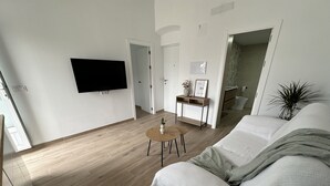 A modern living room with a wooden floor, a white sofa, a coffee table, and a flat-screen TV mounted on the wall. - Private Terrace, Chillout & Outdoor Dining (Alcala De Los Gazules)