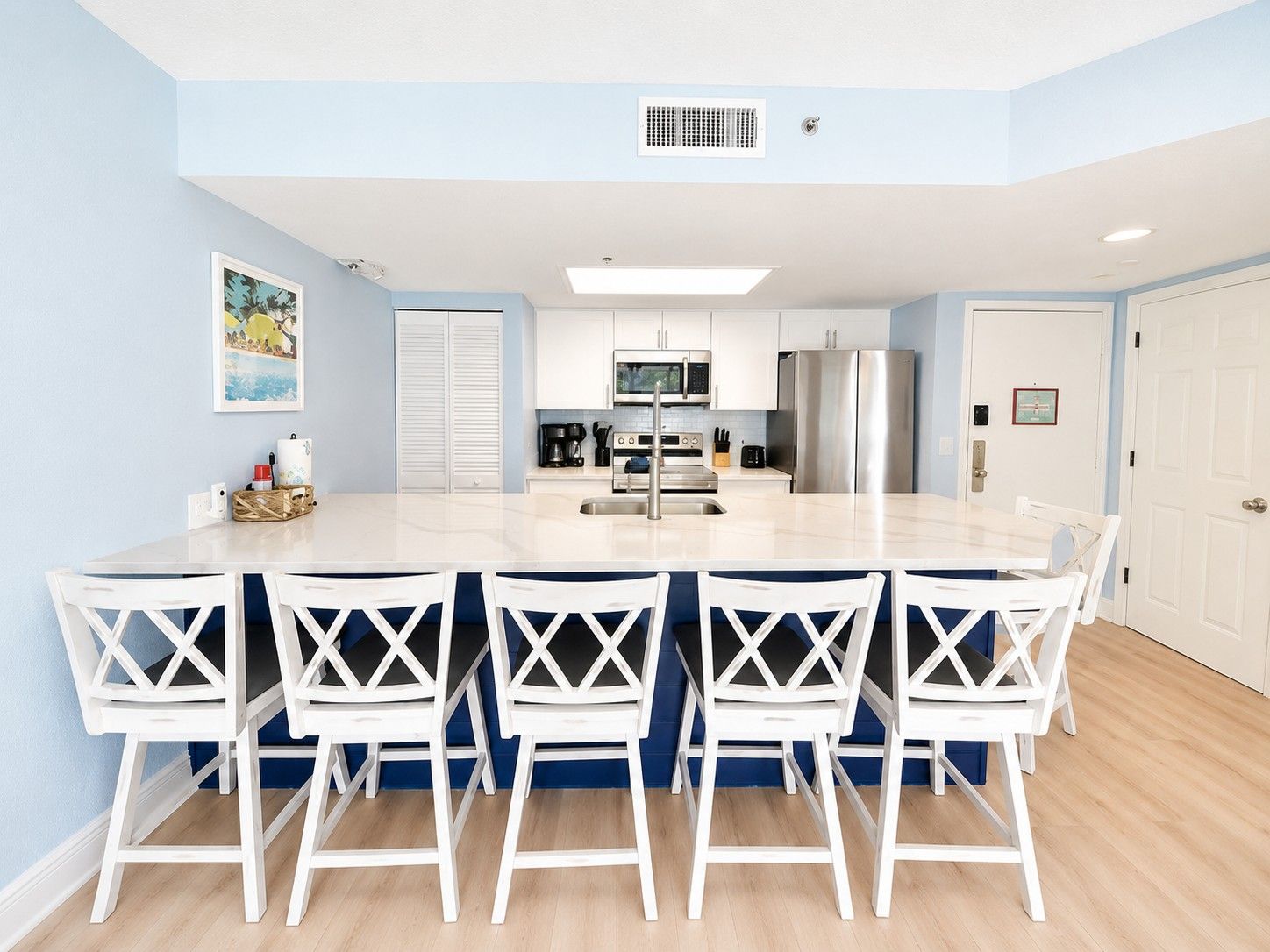 A modern kitchen with a central island, white cabinets, stainless steel appliances, and a dining area with white chairs.