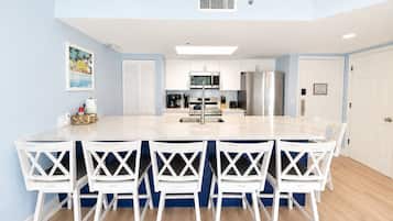 A modern kitchen with a central island, white cabinets, stainless steel appliances, and a dining area with white chairs.