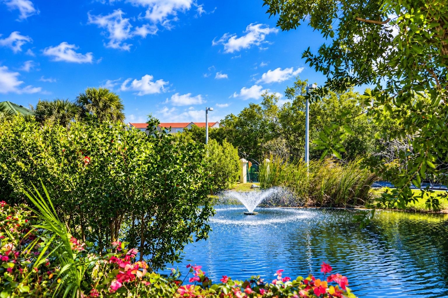 Un jardín tranquilo con una fuente, abundante vegetación y un cielo azul despejado.