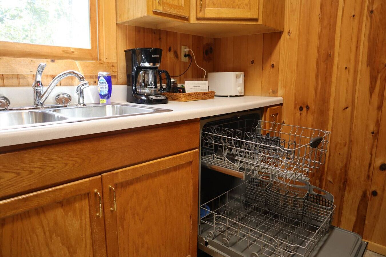 Une cuisine compacte avec des meubles en bois, un évier en acier inoxydable, une machine à café et un lave-vaisselle.