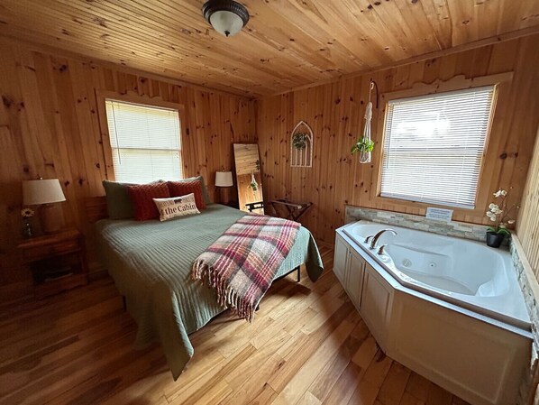 A cabin-style bedroom with a bed, a large window, a bathtub, and wooden walls.
