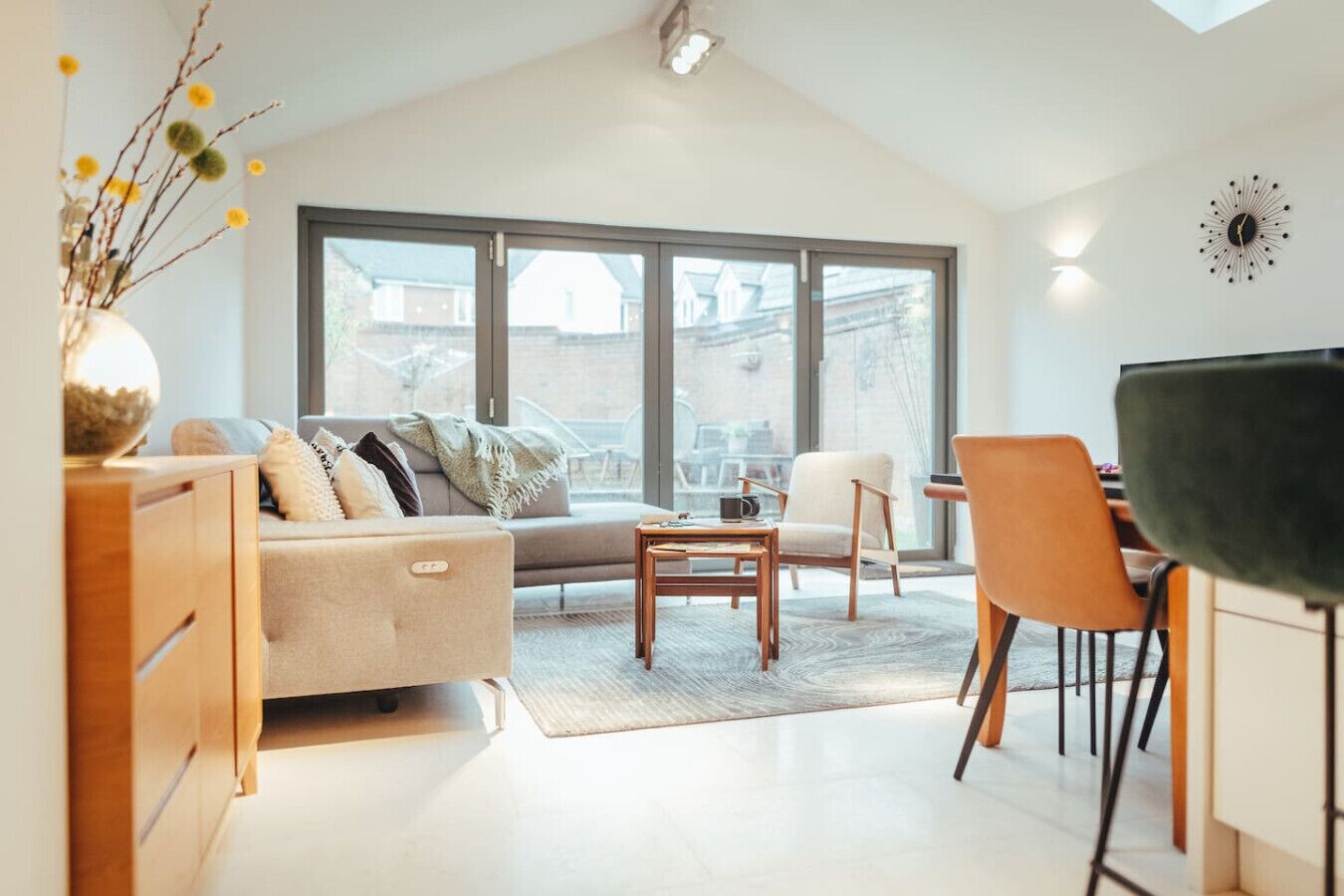 Uma sala de estar moderna com sofá, mesa de centro e cadeiras, grandes janelas e um espaço de jantar.