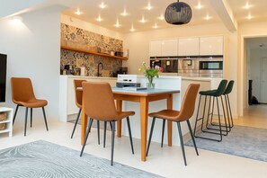 Eine moderne Küche mit weißen Schränken, einem Einbauofen und einer Mikrowelle. Es gibt einen Essbereich mit einem Holztisch und vier Stühlen.