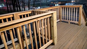 A wooden deck with railings, overlooking a parking area with cars and a billboard in the background. - New Modern 2 BR in Excellent Location (201) (Maryville)