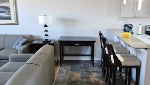 A modern living room with a grey sofa, a black coffee table, and a dining area with a kitchen counter. - New Modern 2 BR in Excellent Location (201) (Maryville)