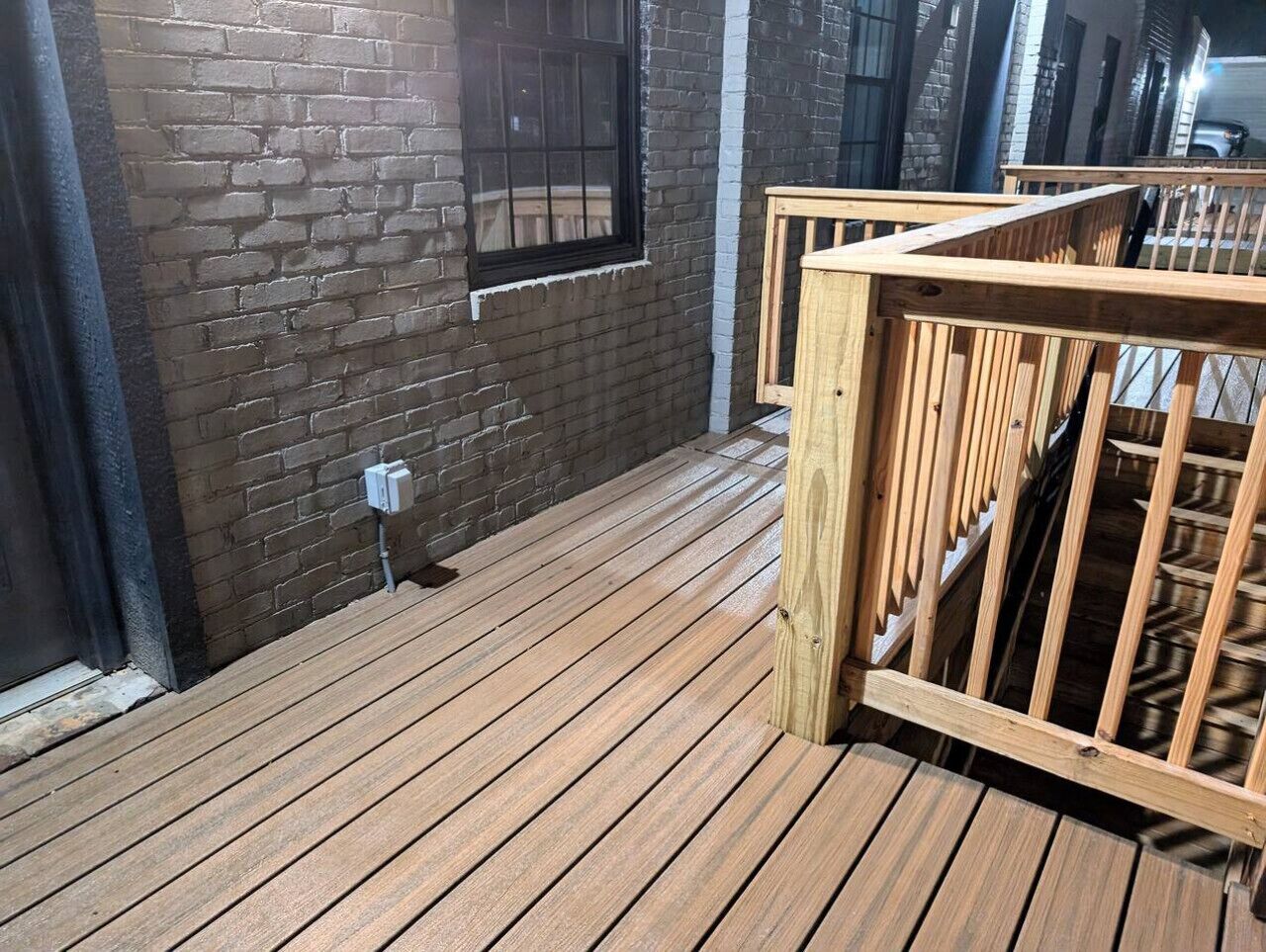 Une terrasse en bois avec un mur en briques et une fenêtre.
