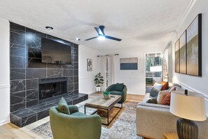 A modern living room with a fireplace, green armchairs, a sofa, and a ceiling fan. - Fayetteville Gem -Pet friendly / near Trilith Studios  (Fayetteville)