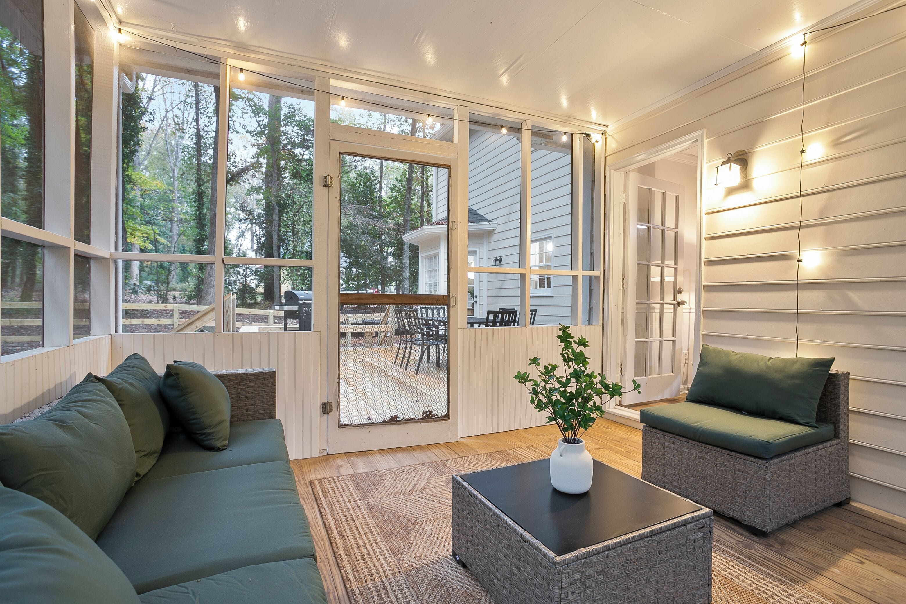 A cozy room with a sectional sofa, a small table, and a chair. There is a sliding glass door leading to an outdoor deck with a table and chairs.