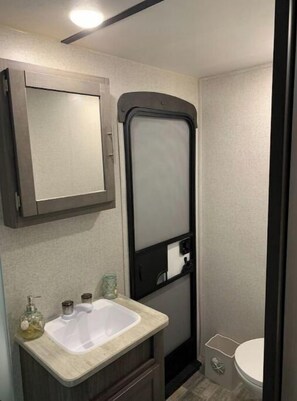 A compact bathroom with a sink, mirror, and toilet.